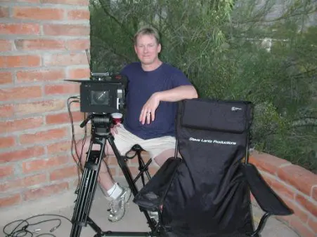 Man with camera and tripod outdoors.