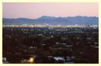 Here's an alt tag for the image: `City lights at dusk, mountains in background`