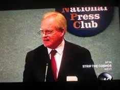 A man in suit and tie speaking at a press conference.